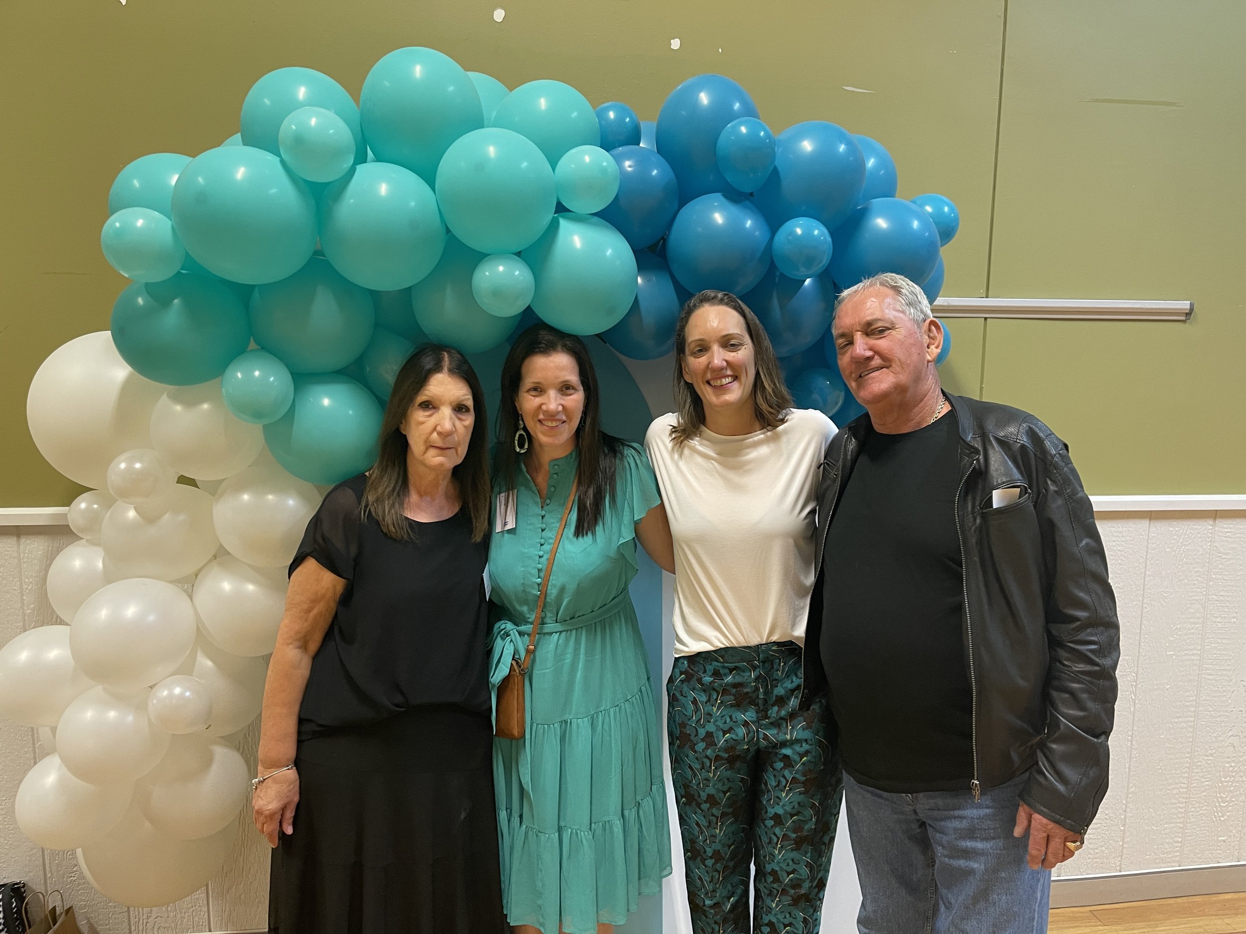 Four people standing in front of a colorful balloon backdrop, smiling.