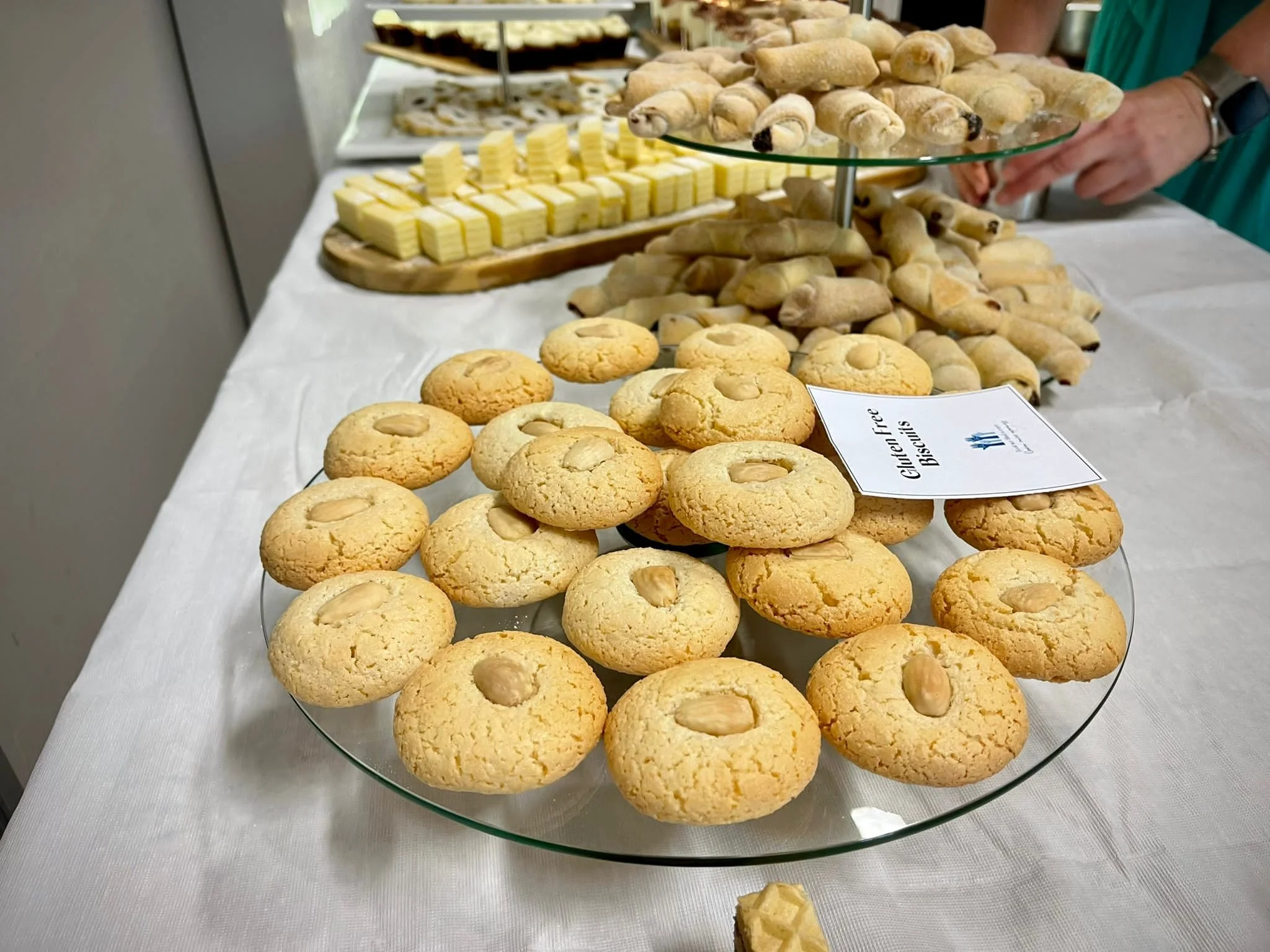 Plate of gluten-free cookies topped with peanuts, part of a buffet of baked goods including cookies, biscuits, and pastries displayed on a white tablecloth.