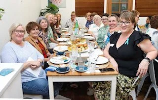 Group of women gathered around a table for a meal or celebration in a warmly decorated room.