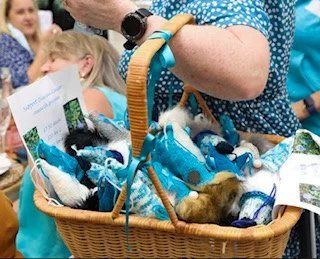 A person holding a basket filled with small animals, possibly puppies or kittens, at an outdoor event.