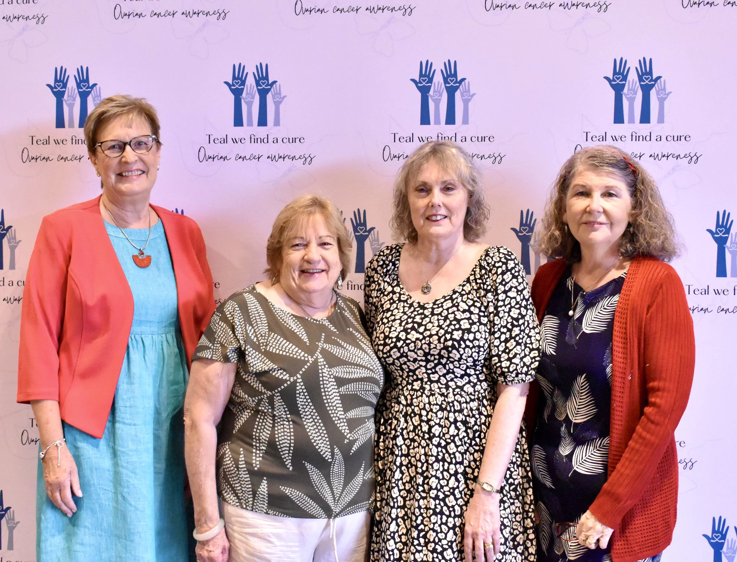 Four women standing in front of a backdrop with logos and text celebrating ovarian cancer awareness.