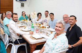 Group of people sitting around a dining table, enjoying a meal together in a bright room.