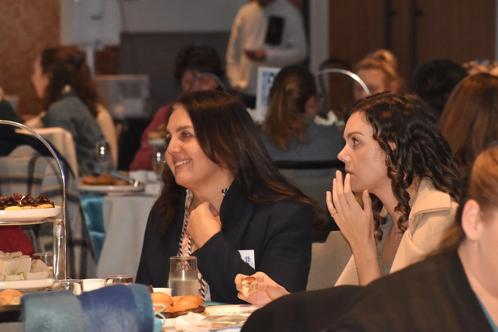 Women seated at a table during a social event with food and beverages, engaging in conversation.