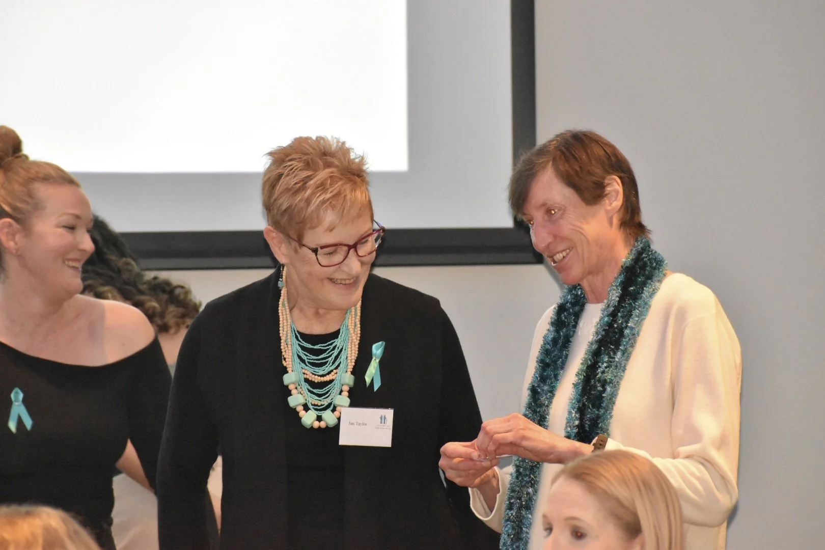 Four women, including two in the forefront, are engaged in a conversation, smiling during an indoor event.