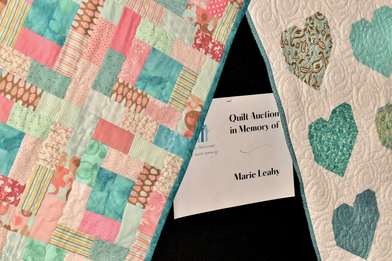 A colorful patchwork quilt with hearts and squares, and a white quilt with heart-shaped patterns; a paper for a quilt auction in memory of Marie Leahy.