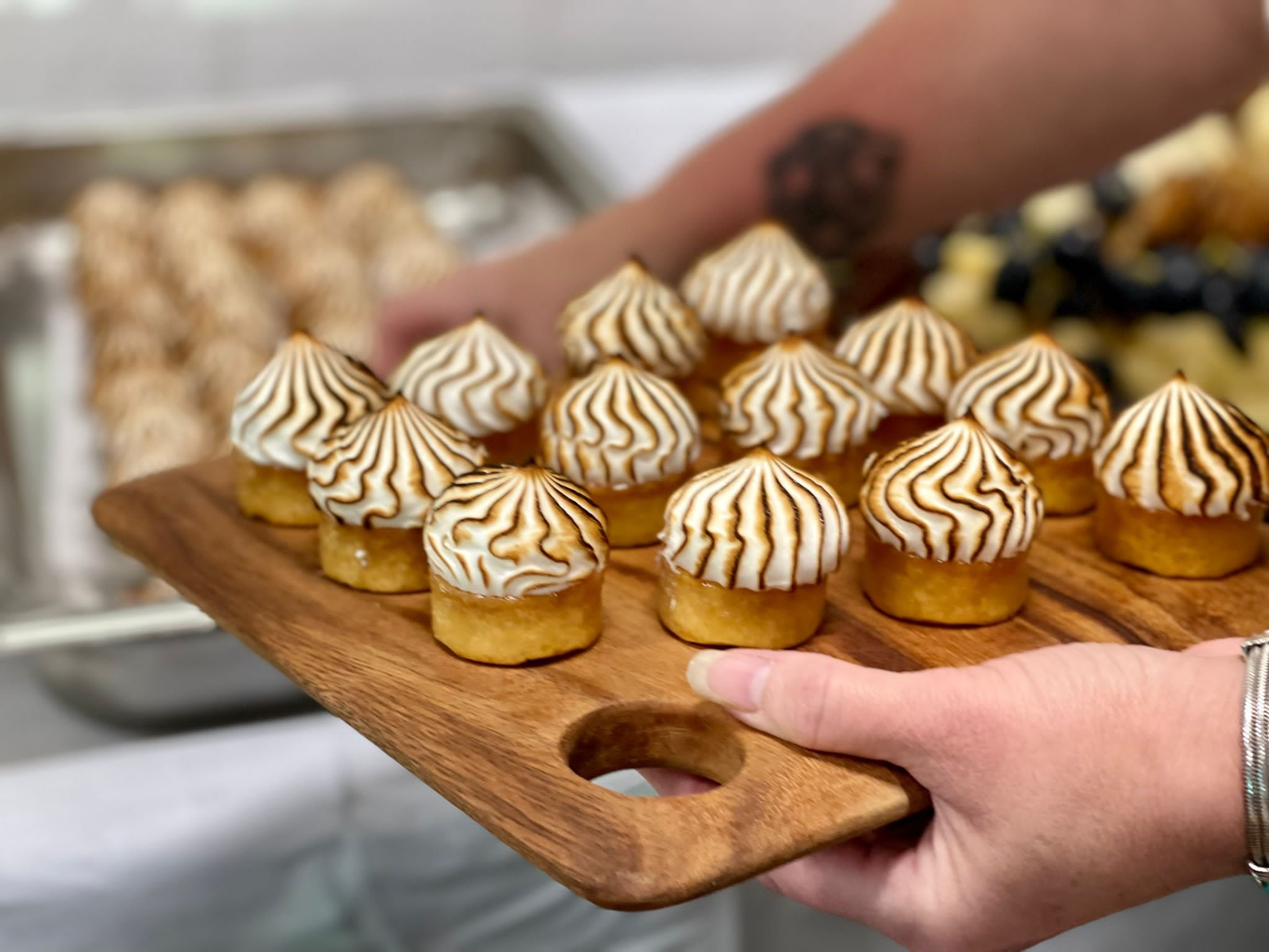 Mini desserts with toasted meringue topping on a wooden serving board, person holding the board