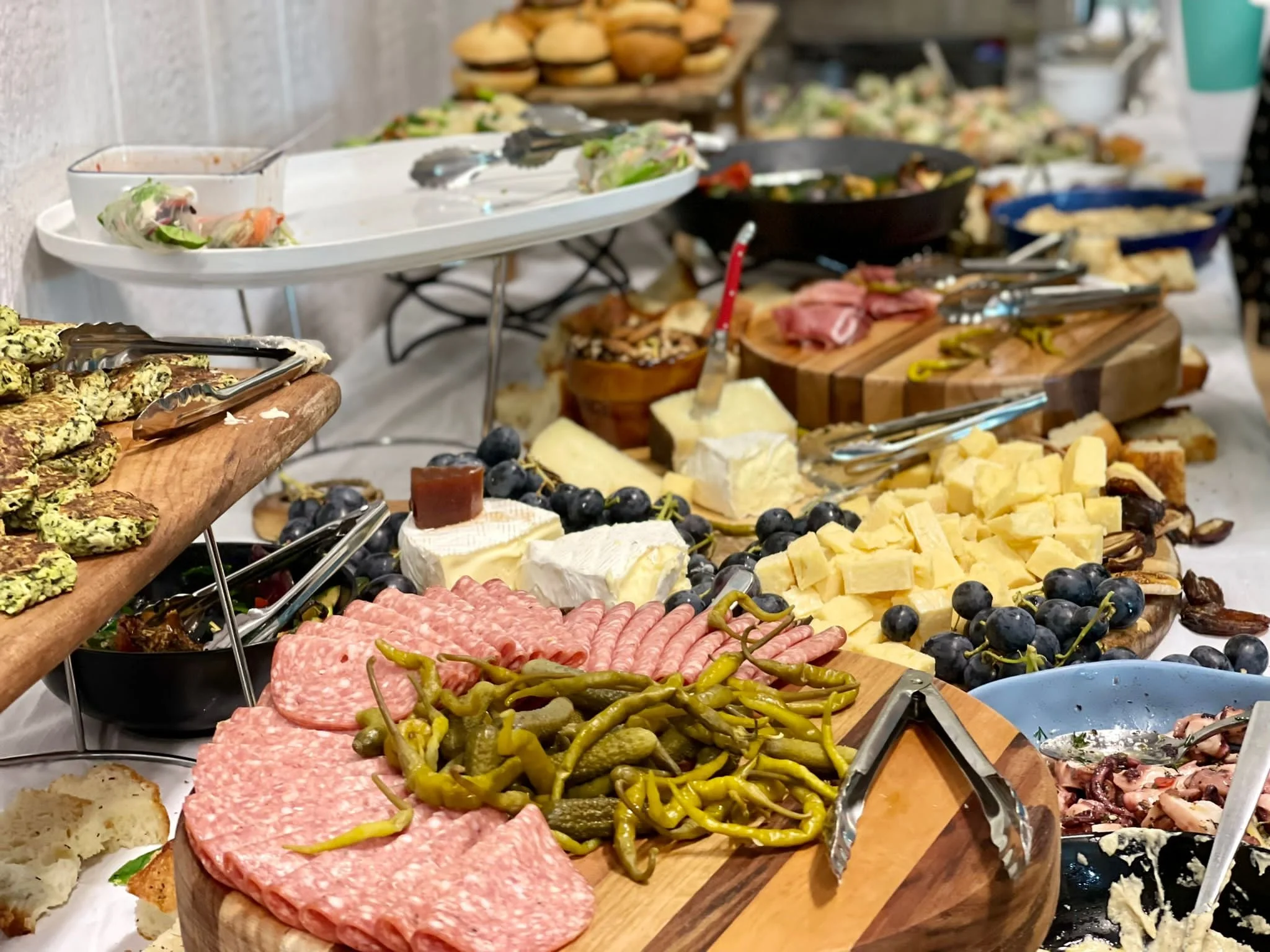 Assorted cheeses, cured meats, grapes, and pickled peppers on a buffet table.