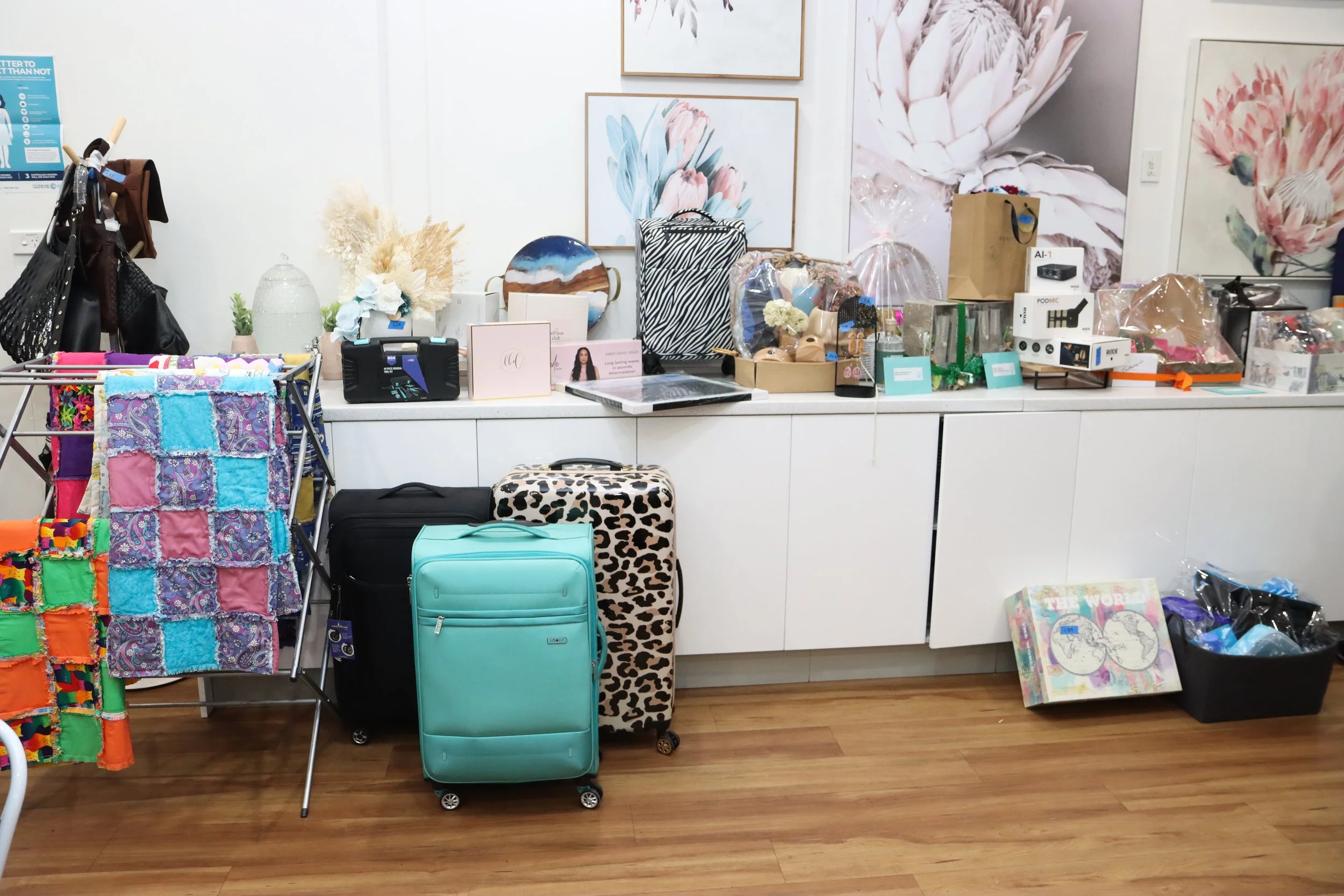 Display of luggage, handbags, decorative items, and assorted gifts on white cabinets, with artwork and decorations in the background.