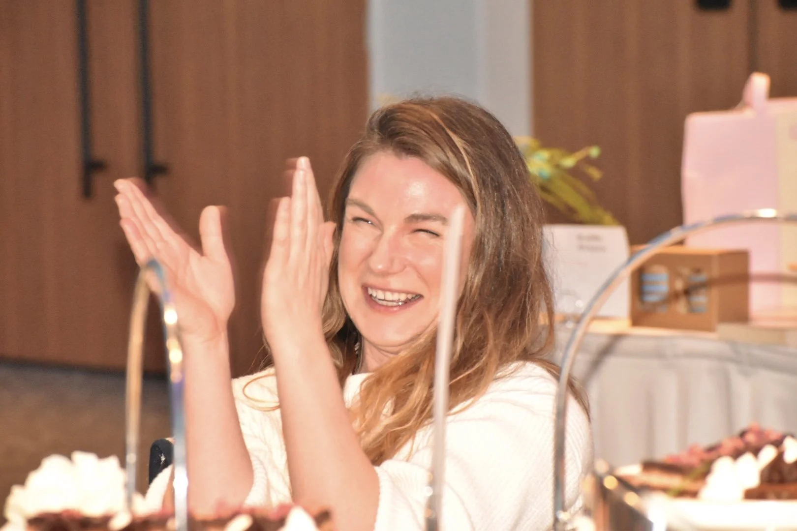 Woman laughing with hands near her face at a bakery or cafe counter.