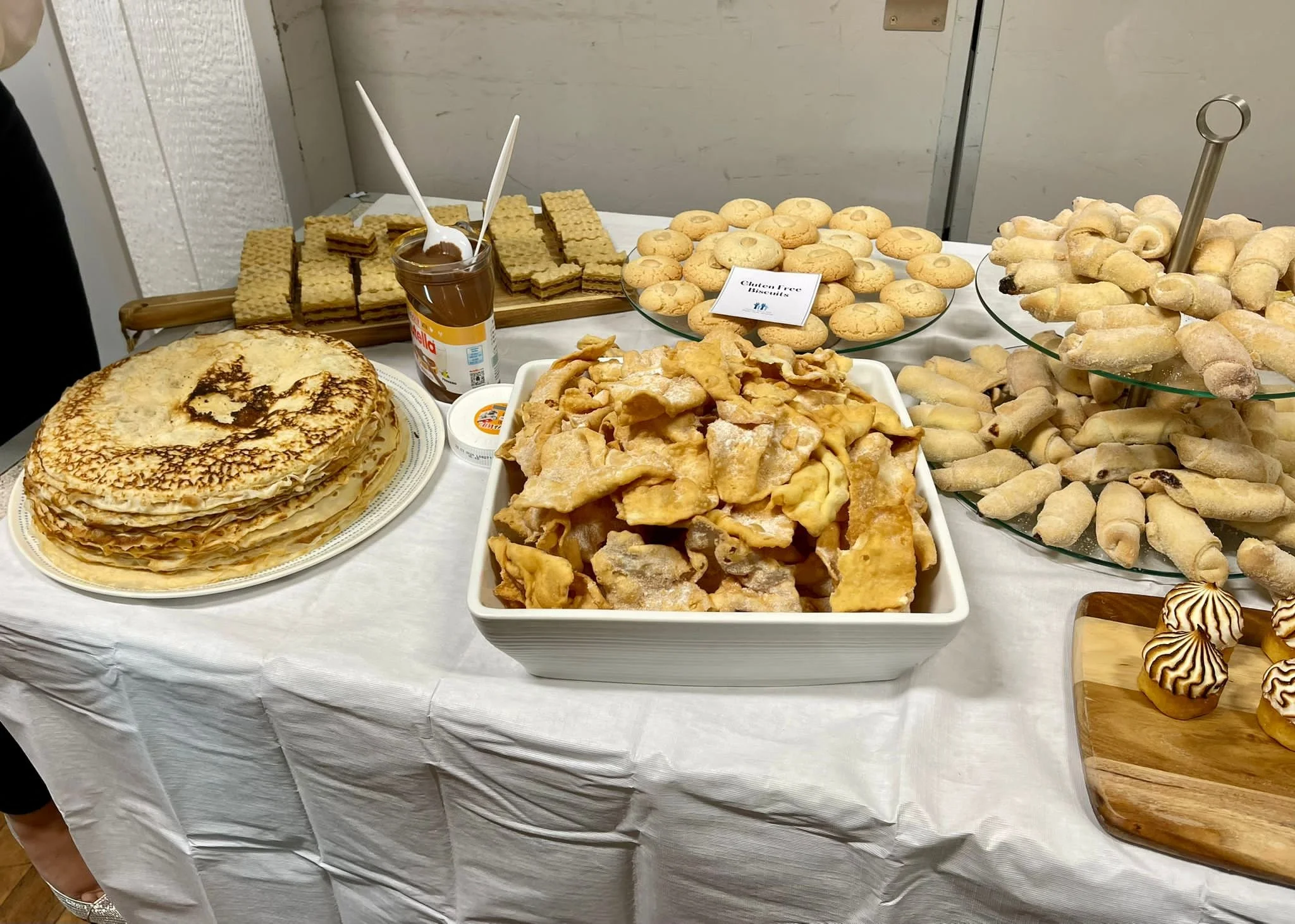 A table with a variety of desserts including crepes, cookies, and pastries, with some labeled as gluten-free