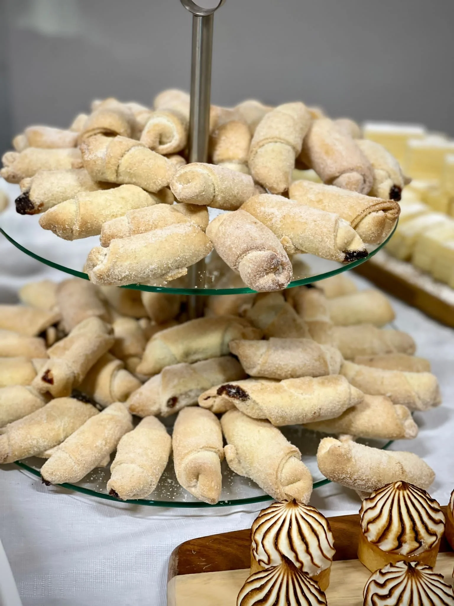 Assorted sugar-coated cookies and baked goods displayed on a tiered glass stand, with some pastries in the foreground.
