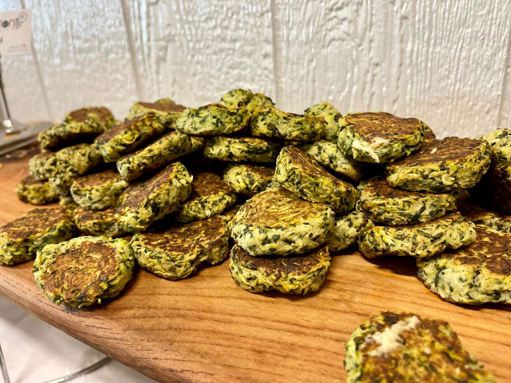 A wooden platter filled with cooked spinach and feta cheese patties.