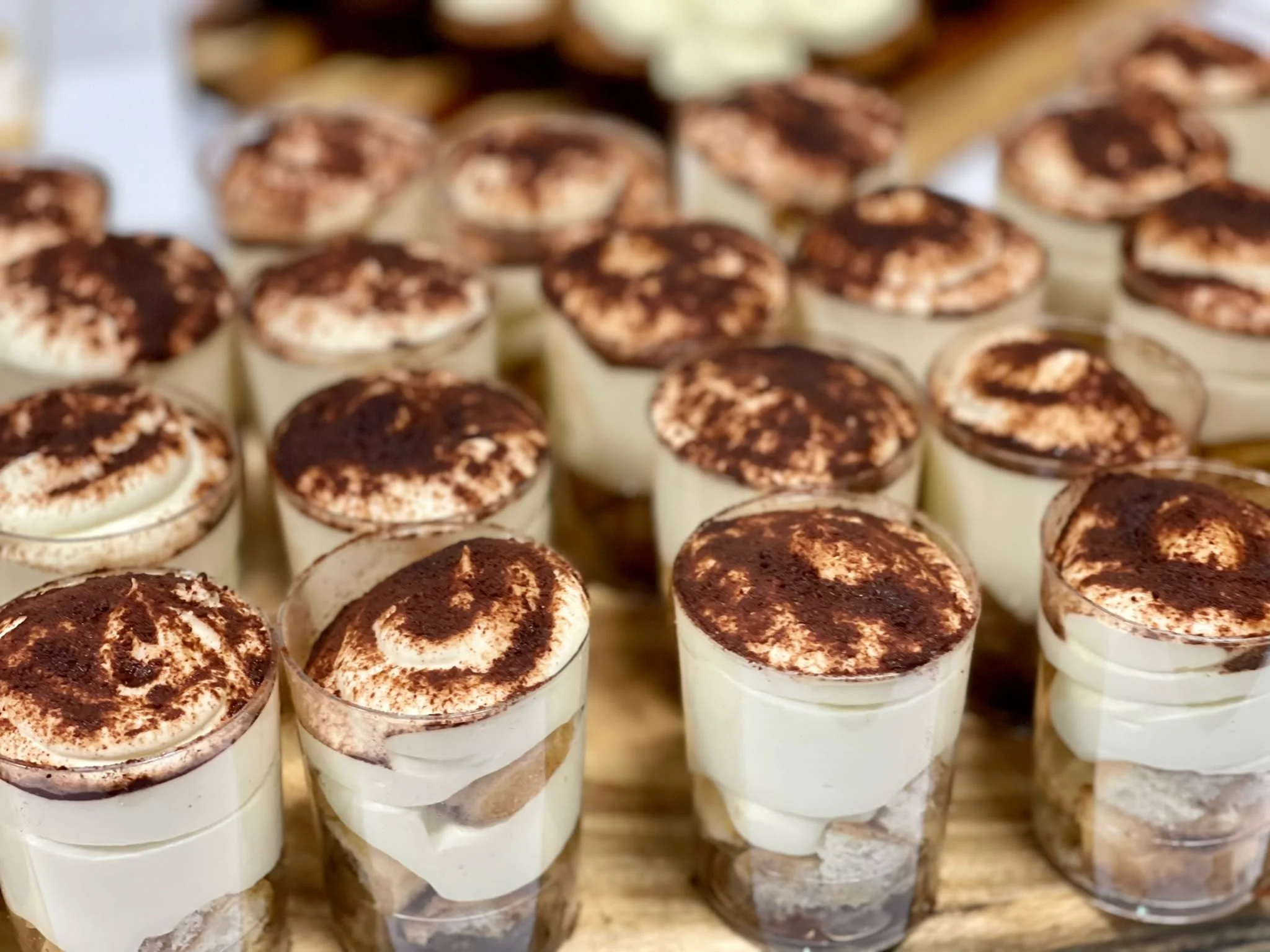 A tray of individual-sized tiramisu desserts in clear cups, topped with cocoa powder.