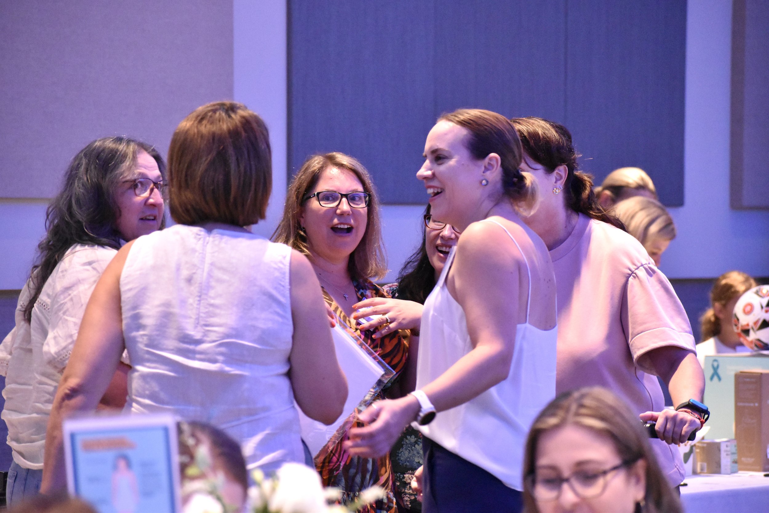 Group of women at a social gathering, laughing and engaging in conversation indoors.