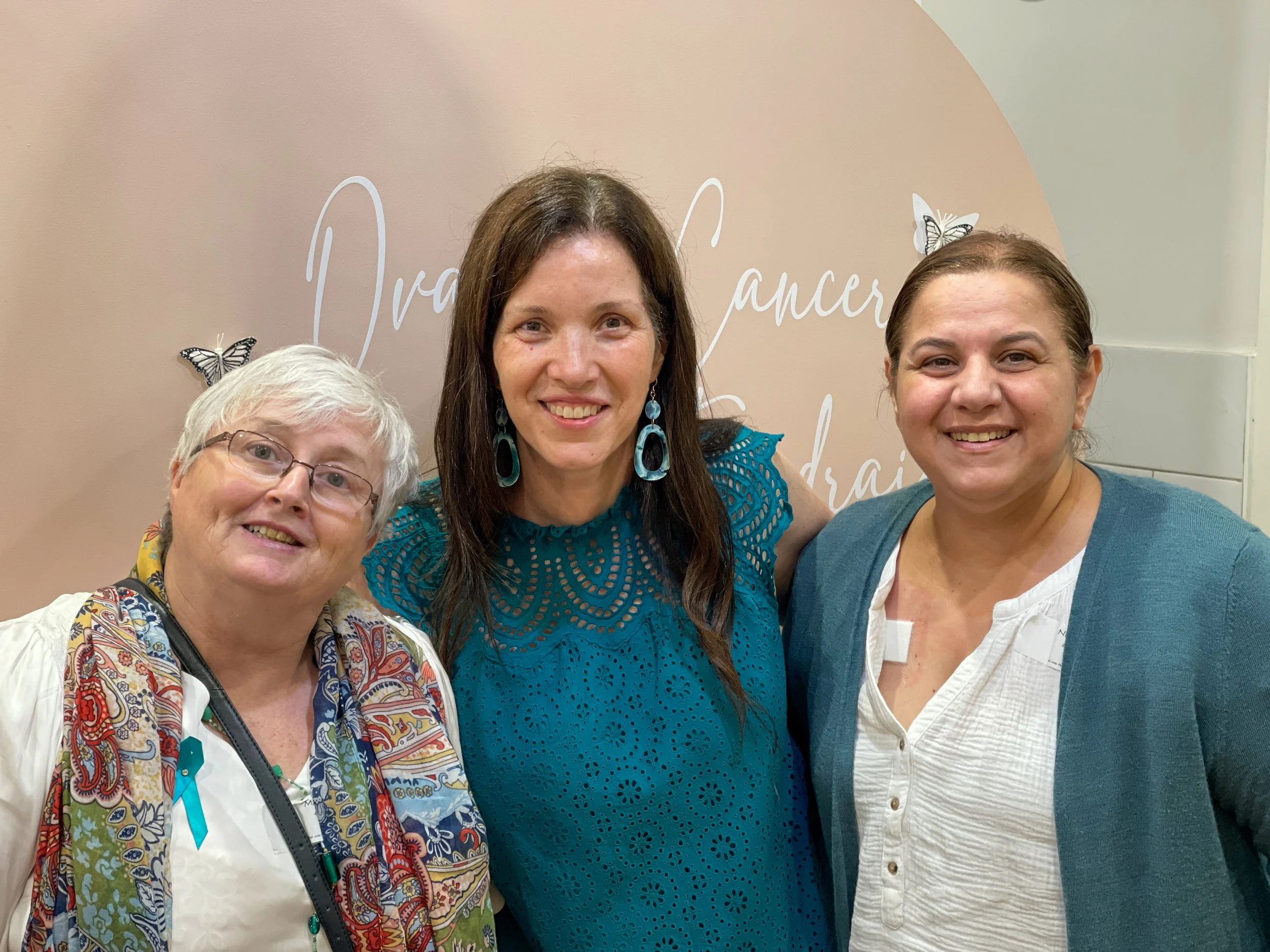 Three women smiling at a breast cancer awareness event.