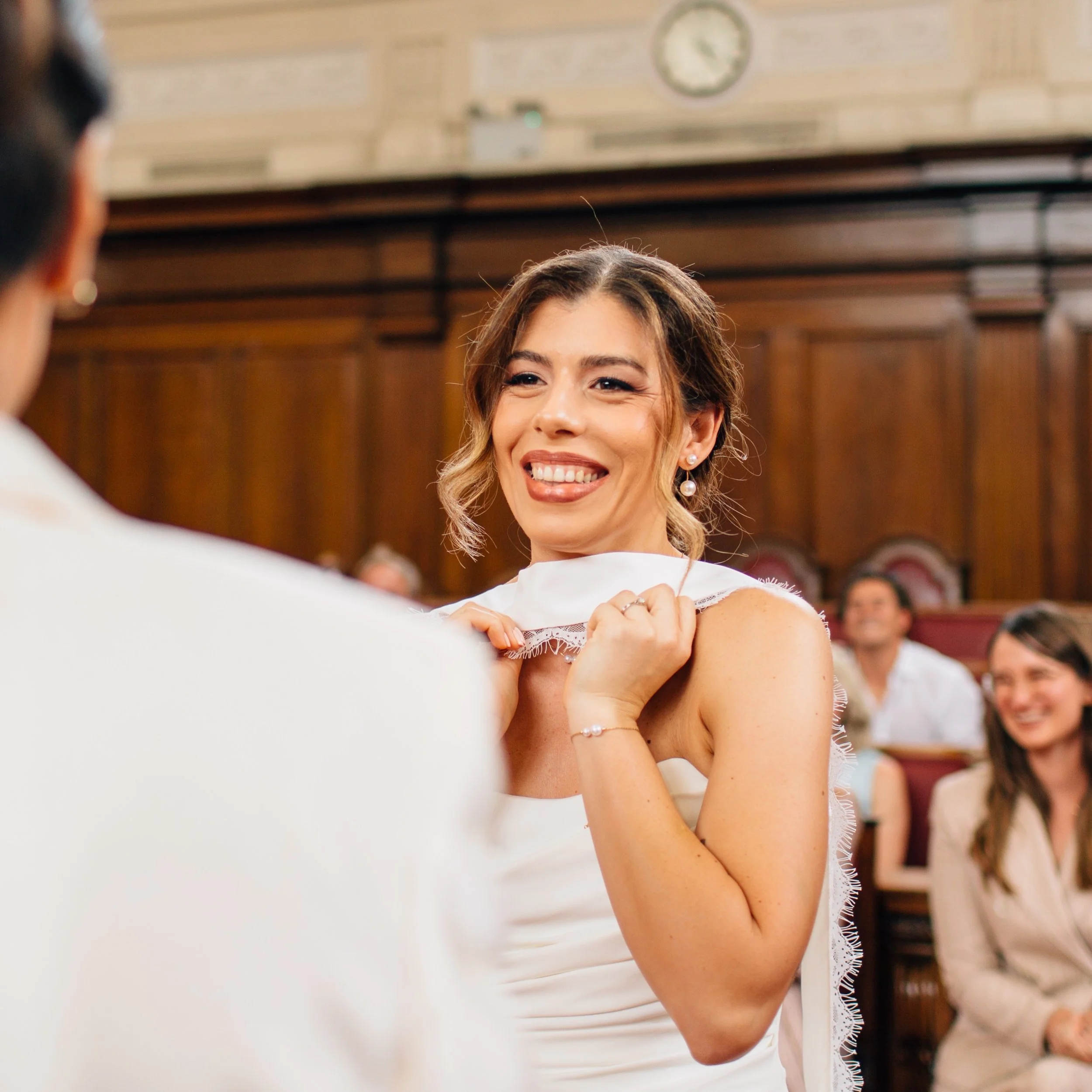 A woman with light brown hair and earrings smiling in a formal setting, possibly at a ceremony or event.