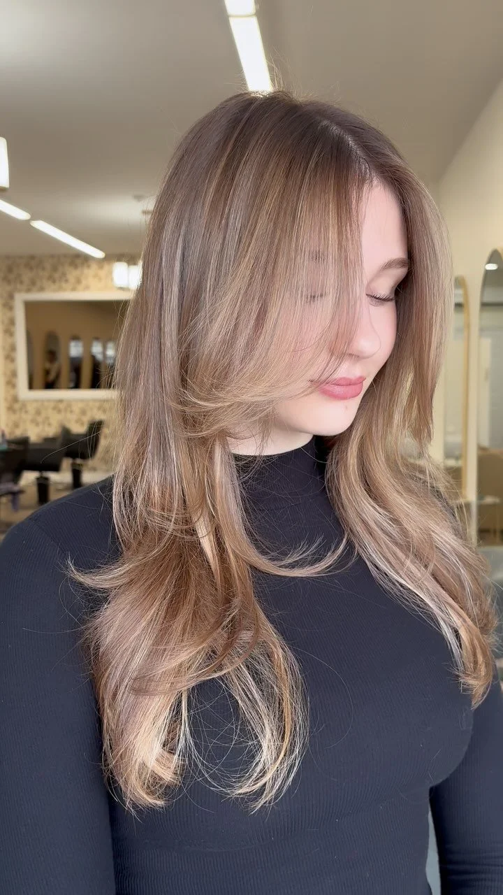 Woman with long wavy blonde hair wearing a black top in a salon.