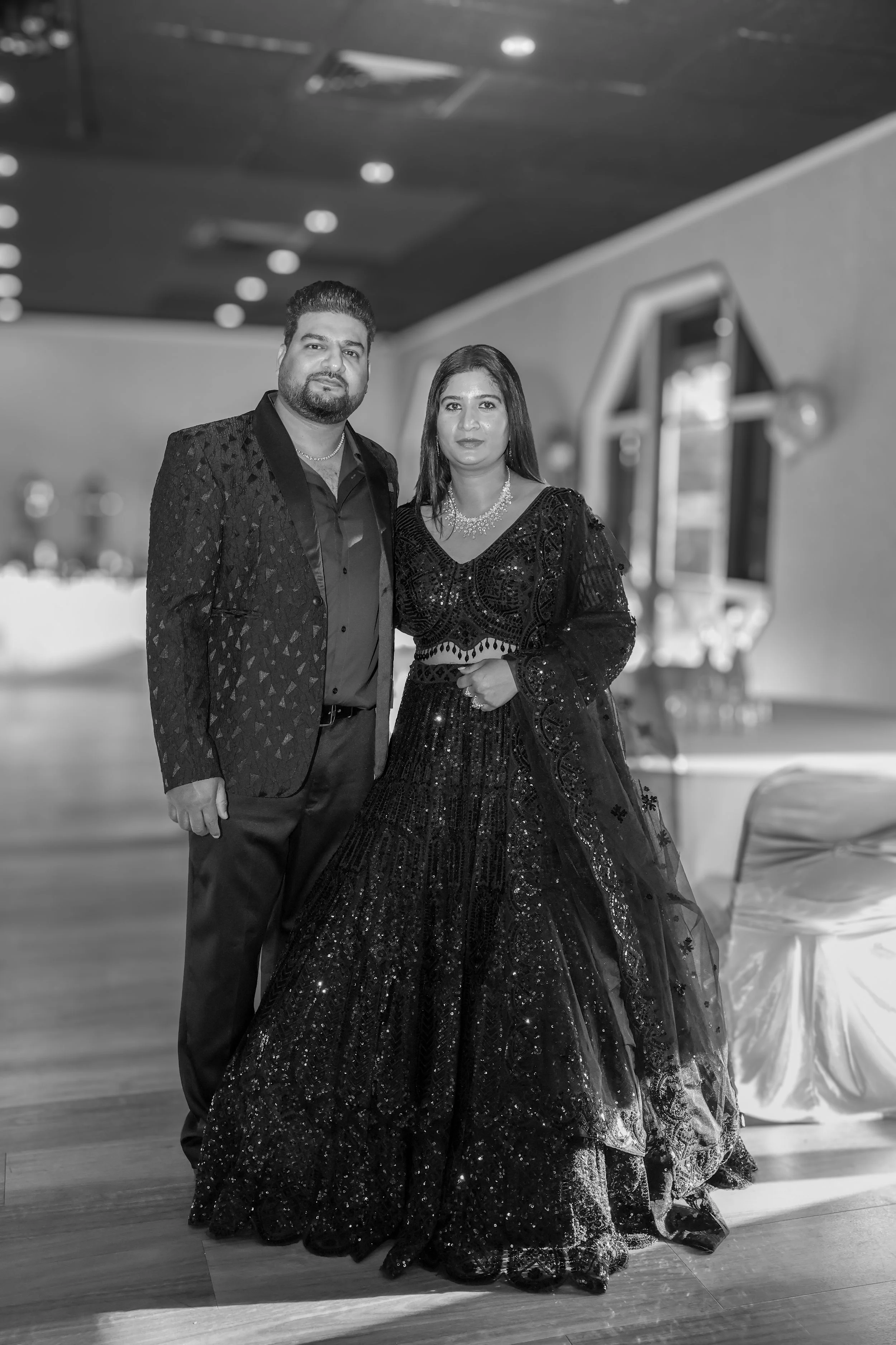 A man and woman dressed in formal attire posing inside a decorated venue.