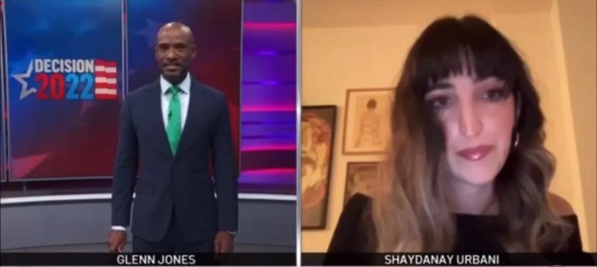Split-screen view of a man in a suit and a woman with dark hair and makeup, participating in a virtual interview or discussion.
