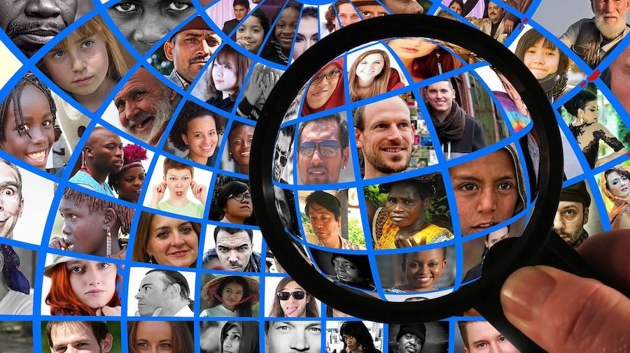 A collage of diverse faces viewed through a magnifying glass, representing global human diversity.