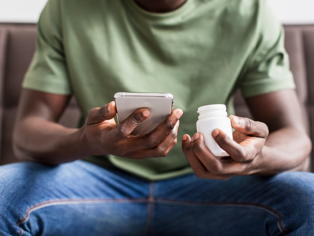 Person in green shirt holding a smartphone and a white medicine bottle.