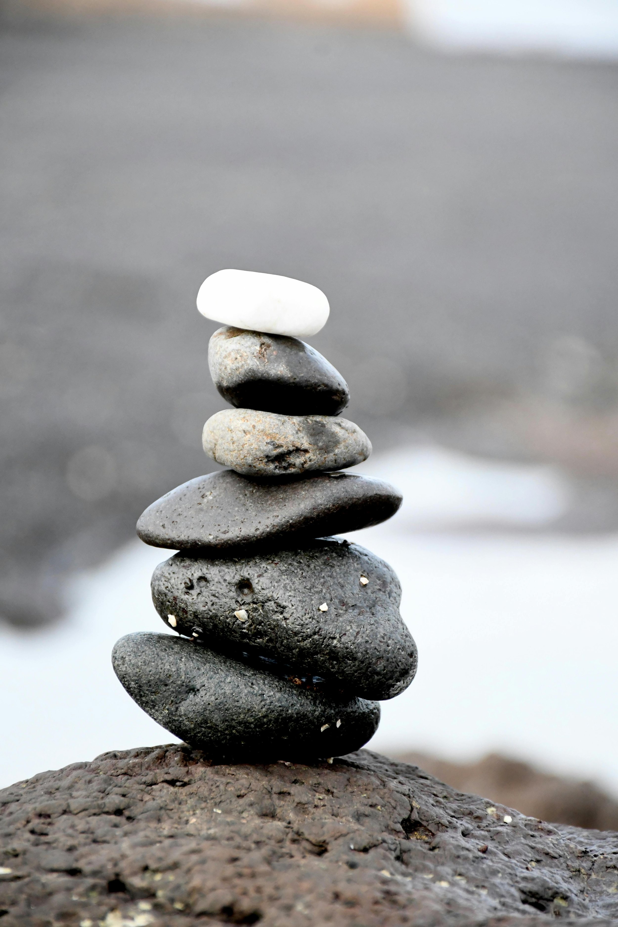 Stacked black, gray, and white stones balanced on a larger rock in a natural outdoor setting with blurred background.