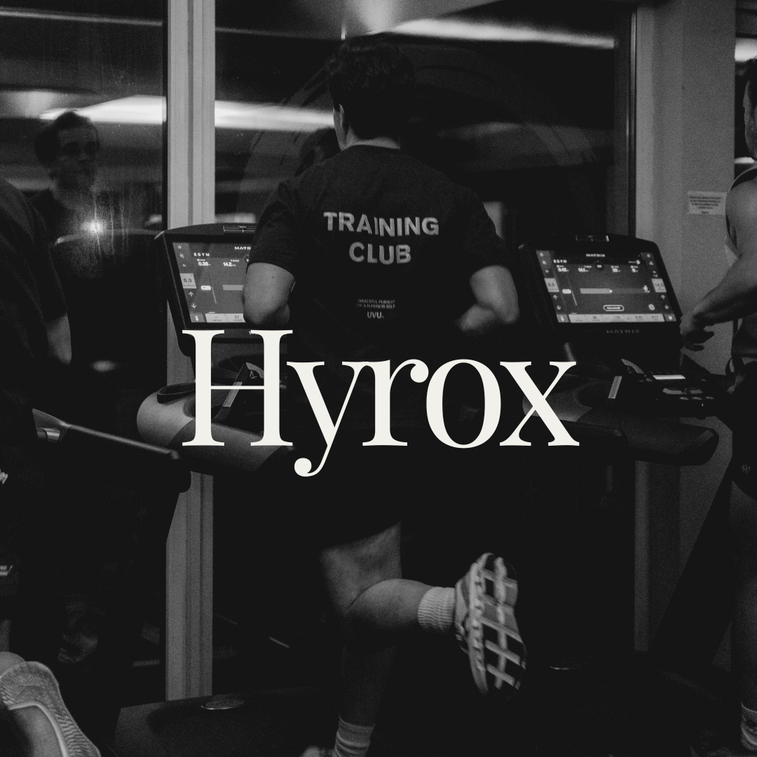 Een person die op een loopband rent in een fitnessruimte, met een sportshirt dat 'TRAINING CLUB' zegt. De foto is zwart-wit en bevat de tekst 'Hyrox' in grote letters over de afbeelding.