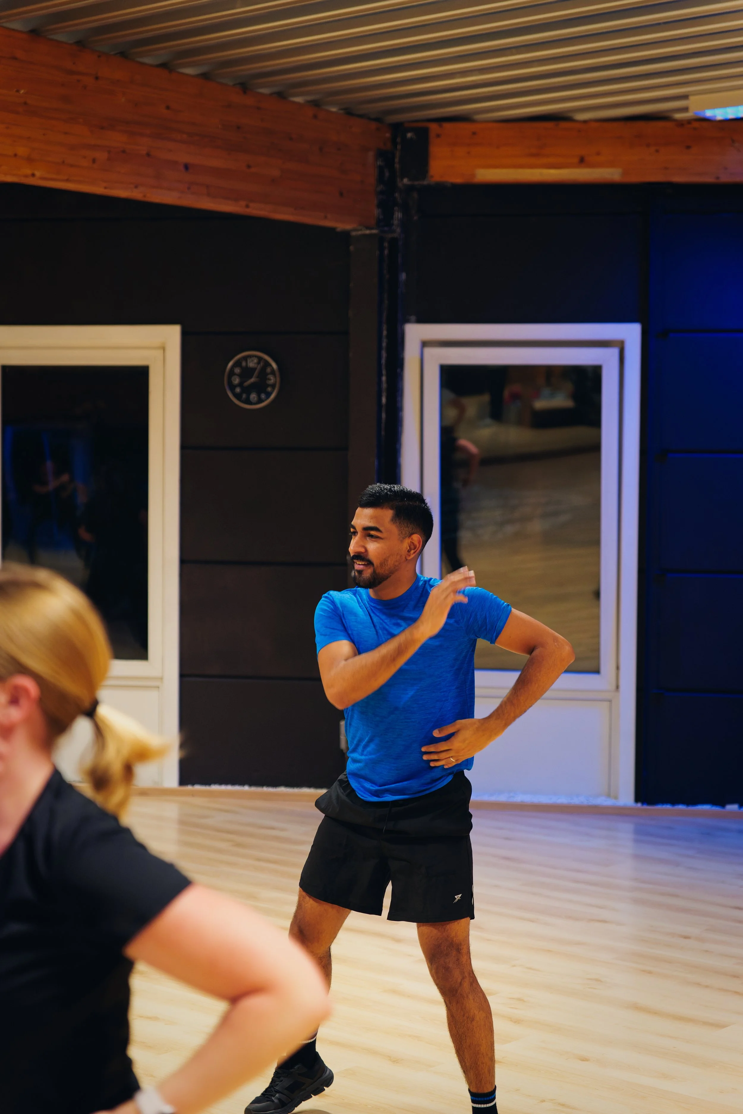 Man in blauwe sportkleding die instructies geeft of danst in een sportschool of dansstudio.