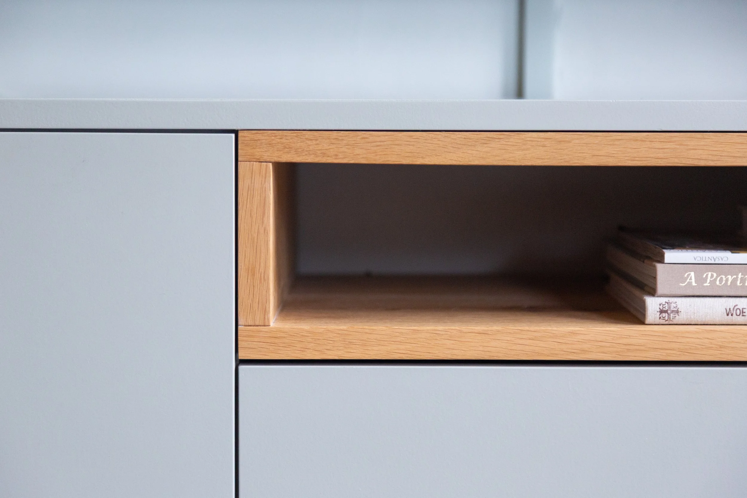 Close-up van een moderne schoenenkast met een lade in lichtgrijs en een open vak met houten afwerking, waarin boeken liggen.