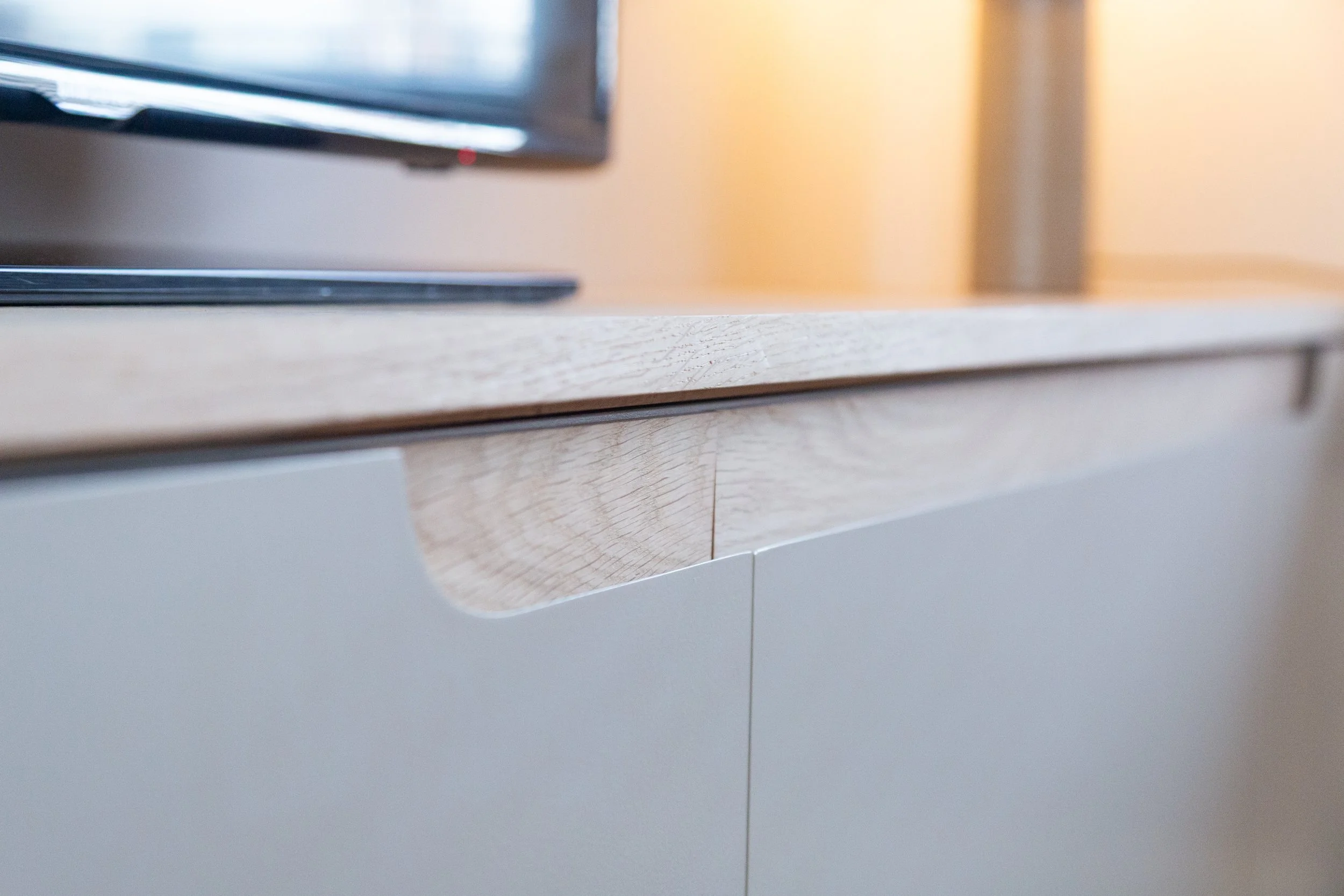 Close-up van een tv-meubel met custom made grepen. Gemaakt van gelakt mdf met een eiken blad.