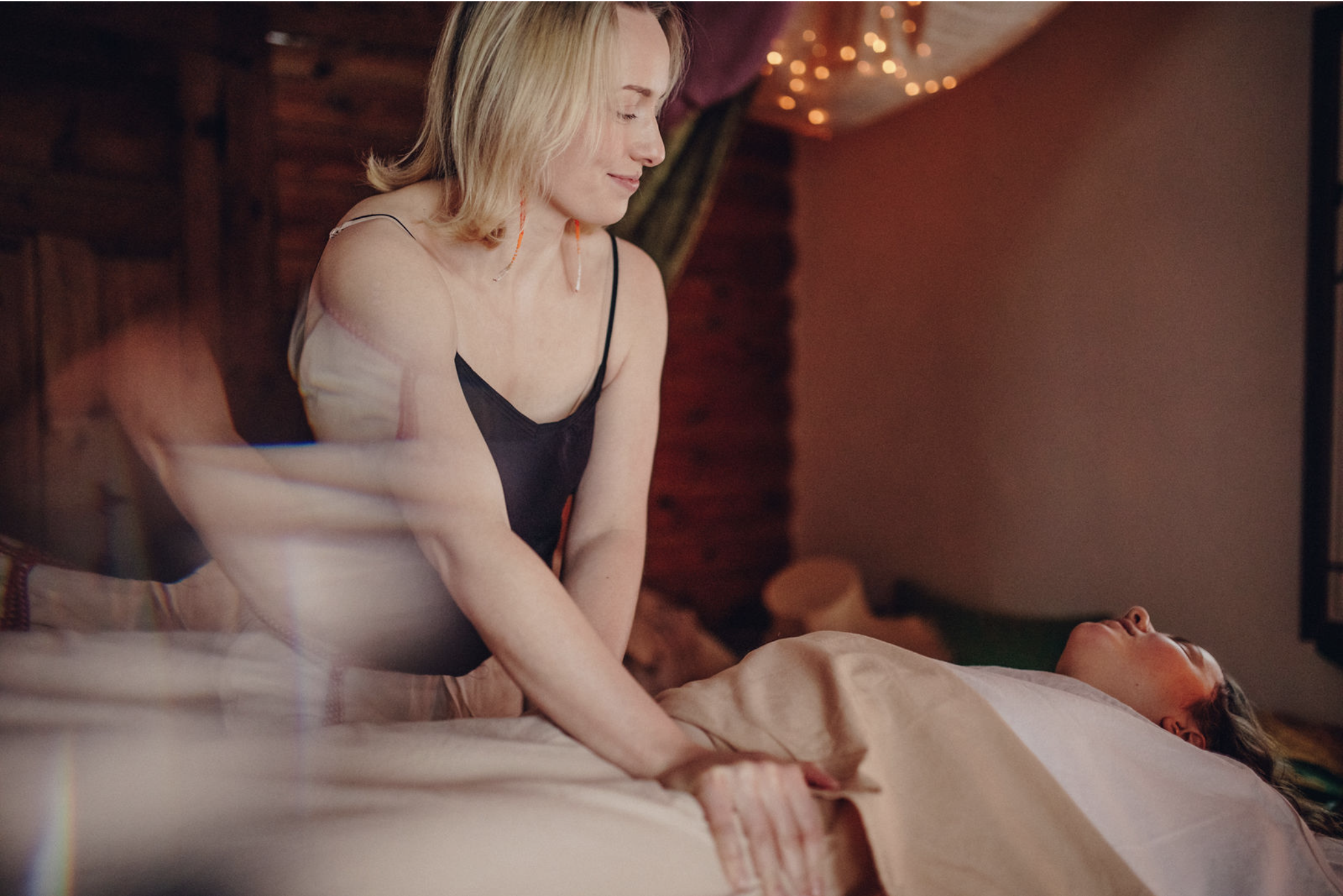 Soojalt valgustatud ja haldjatuledega toas on naine massaažilaual lamava inimese kõrval, hoiab käsi tema kõhul ja vaatab talle õrna ilmega alla