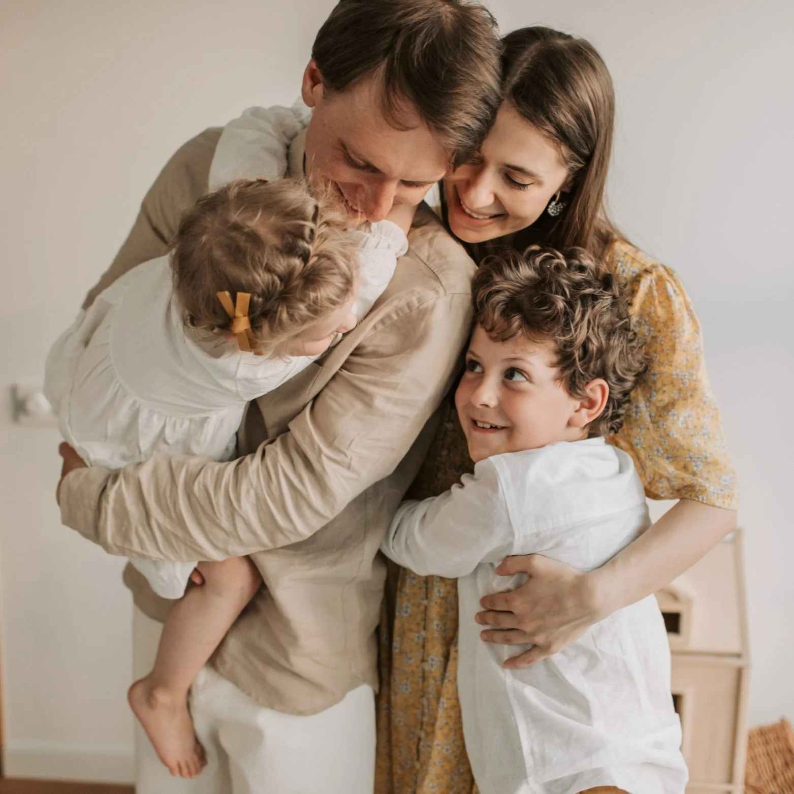 A smiling family of four hugging each other in a cozy indoor setting.