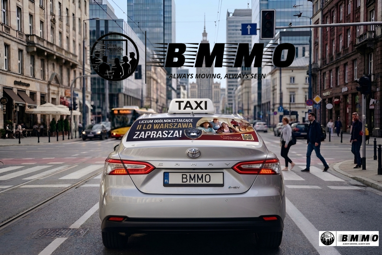 A silver Toyota Camry taxi driving through a busy city intersection during daytime, with pedestrians crossing and tall buildings in the background.