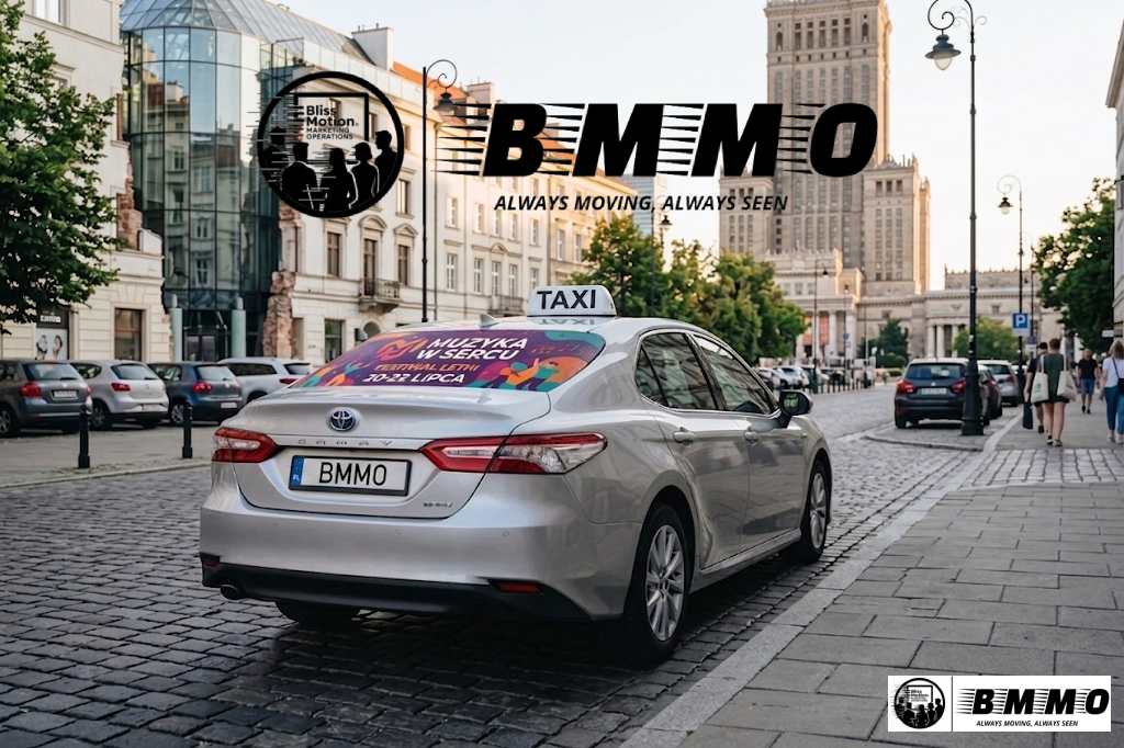 A silver Toyota taxi with a BMMO branded sign on the roof, parked on a cobblestone street in an urban area with tall buildings and pedestrians.