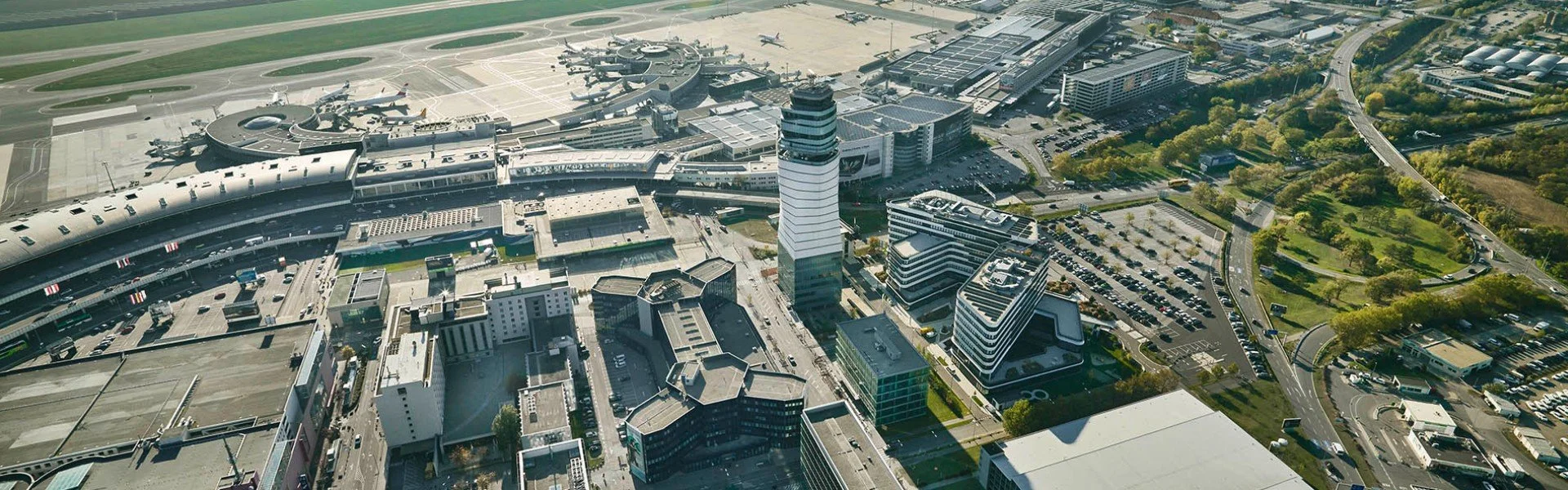 Aerial view of a city airport with multiple runways, airplanes, and surrounding buildings, roads, and green spaces.