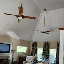 Living room with two ceiling fans, large window with patterned curtains, and TV on the wall.