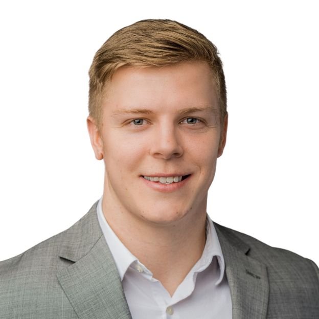 A smiling young man with blond hair wearing a light gray suit and white shirt against a white background.