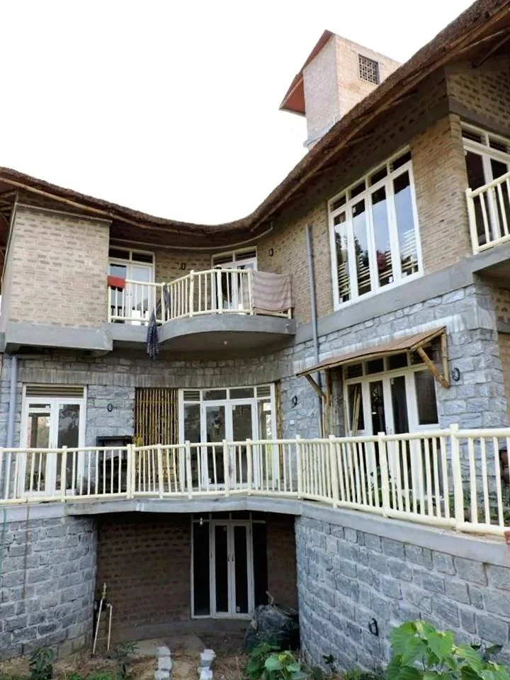 Multi-story brick and stone house with curved balconies and large windows, some with railings and a towel hanging, and a small garden area at the bottom.