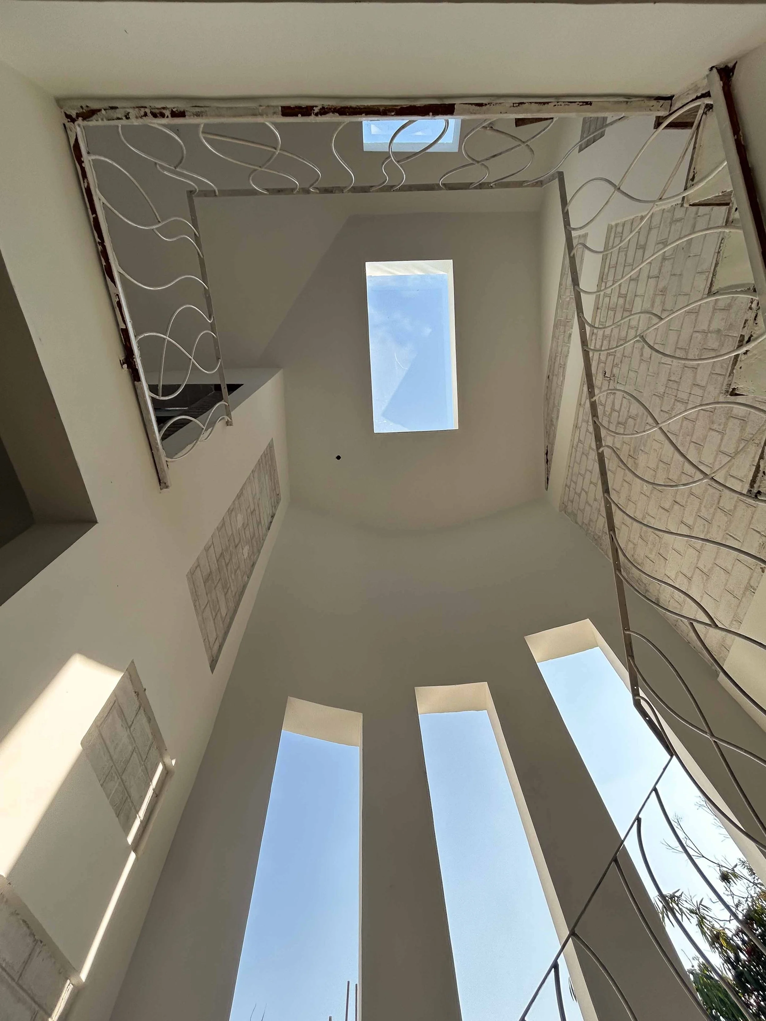 Construction site with an indoor skylight and window, unfinished interior walls, and decorative metal railing.