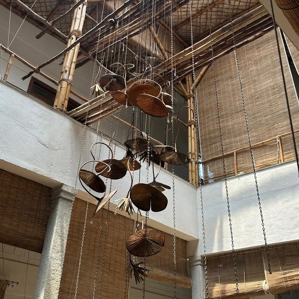 Indoor space with bamboo railings and a hanging mobile made of metal and natural materials, resembling leaves or shells, suspended by chains.