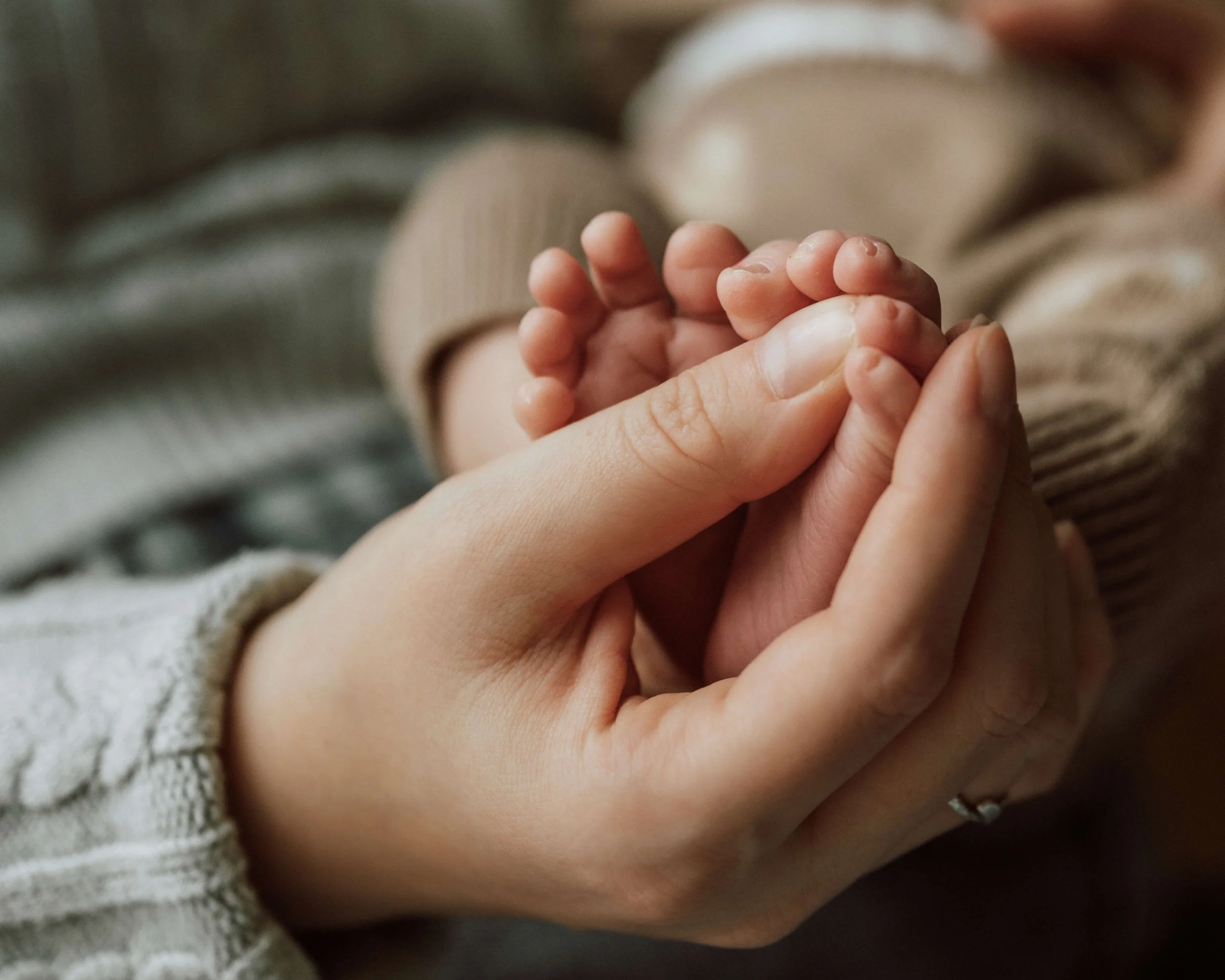 Close-up of an adult hand holding a small child's hand, with both hands visible and the child's hand appearing tiny and delicate.
