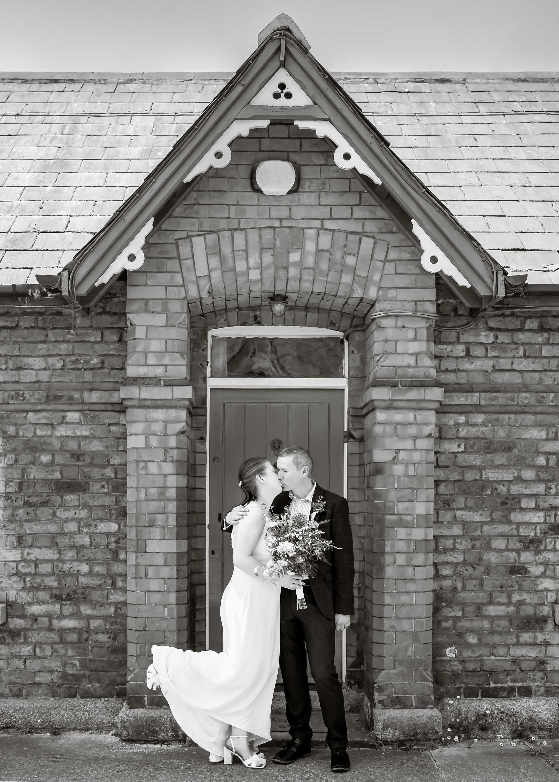 A bride and groom kissing in front of a brick house.