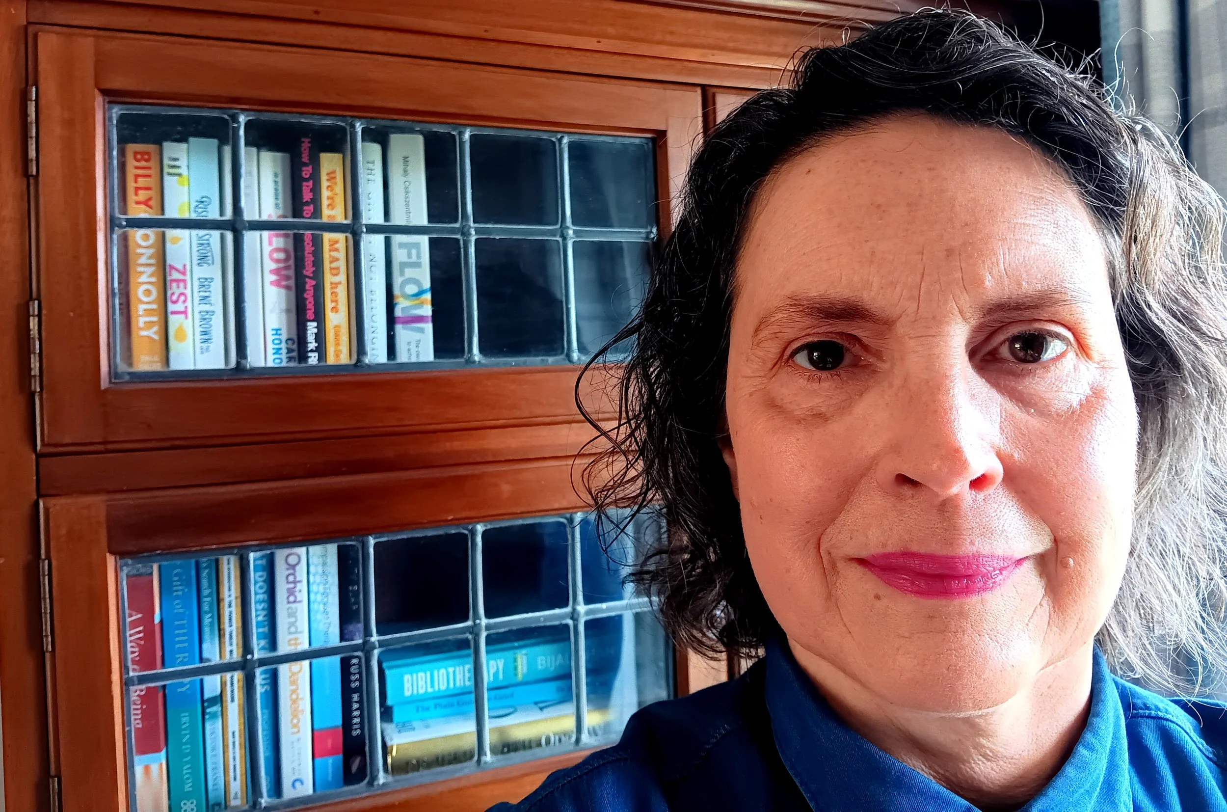 A woman with dark hair in front of a wooden bookshelf filled with books.