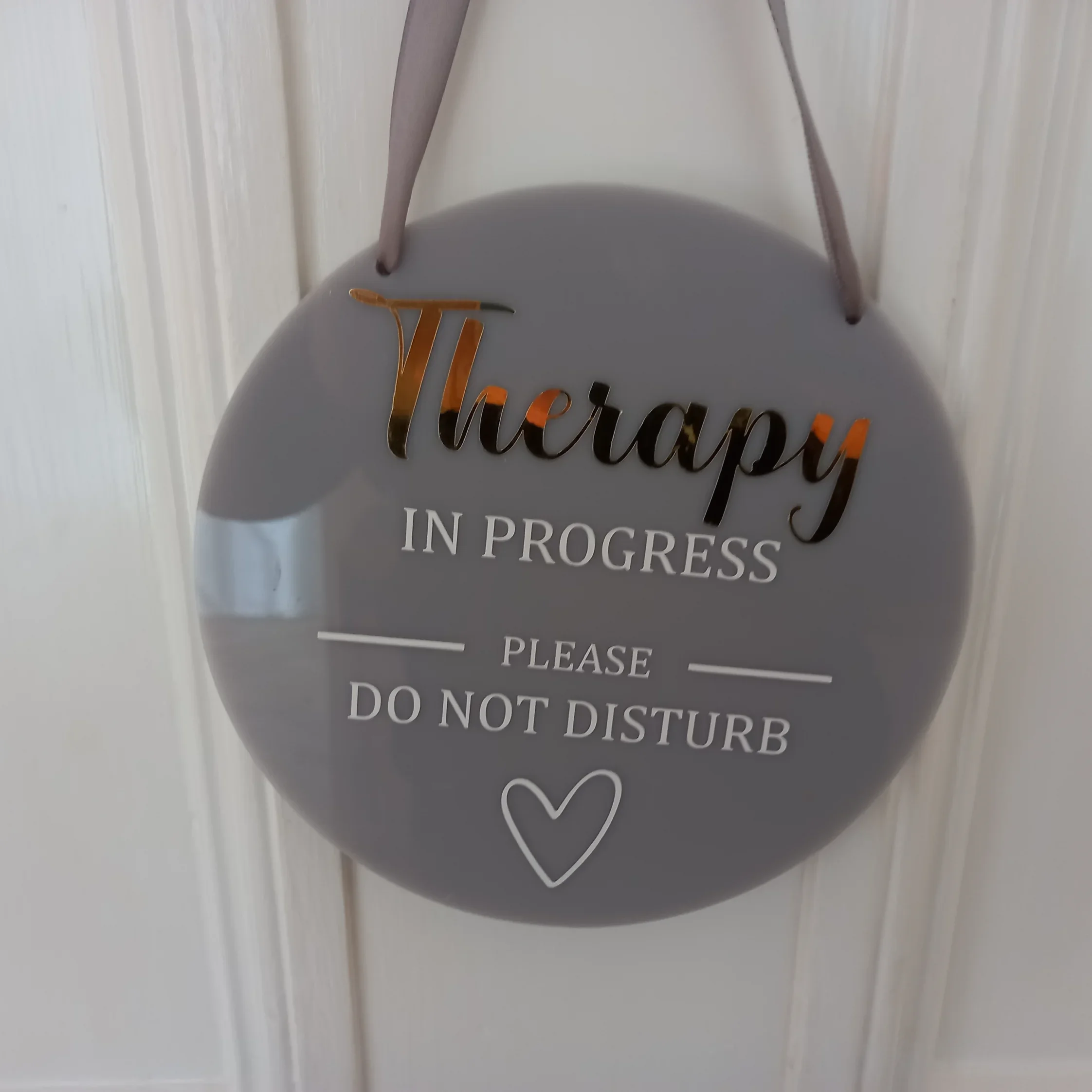 Circular sign hanging on a door that reads 'Therapy in Progress, Please Do Not Disturb' with a heart symbol at the bottom.