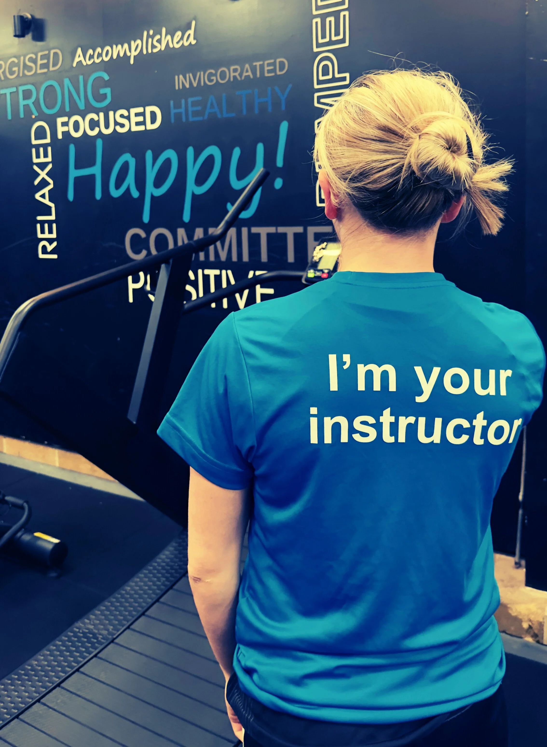 Scenic view of a large mountain range behind a turquoise lake, with rolling green hills and sparse trees in the foreground under a cloudy sky.