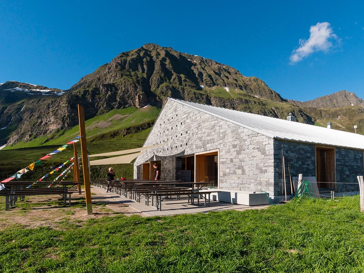 Edificio moderno in pietra con tetto bianco, situato in montagna, con prati e montagne sullo sfondo