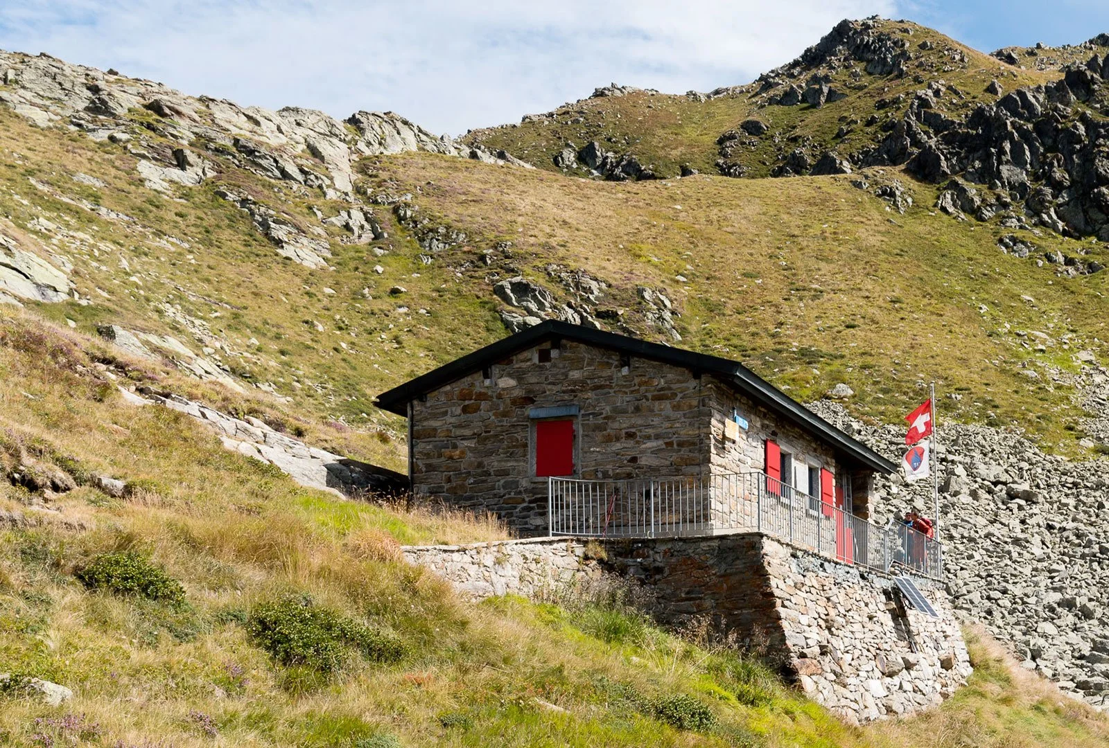 Casa di pietra con bandiera svizzera in un ambiente montano con erba e rocce