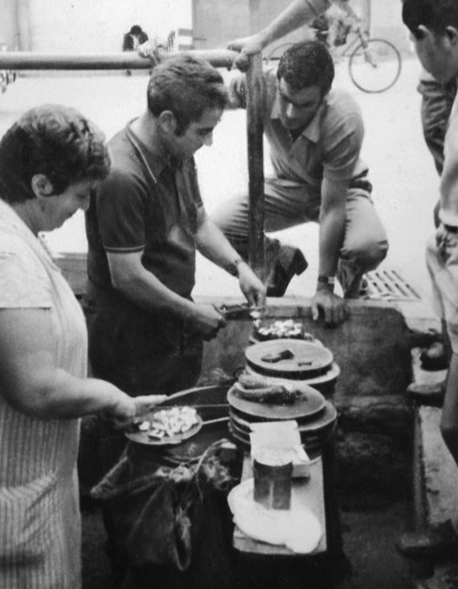 Hombres sirviendo comida en un puesto callejero de tacos.