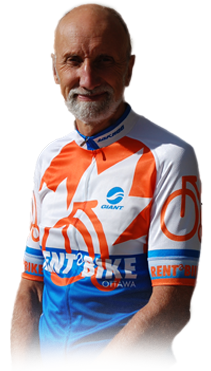 Older man smiling in a cycling jersey with orange, white, and blue colors.