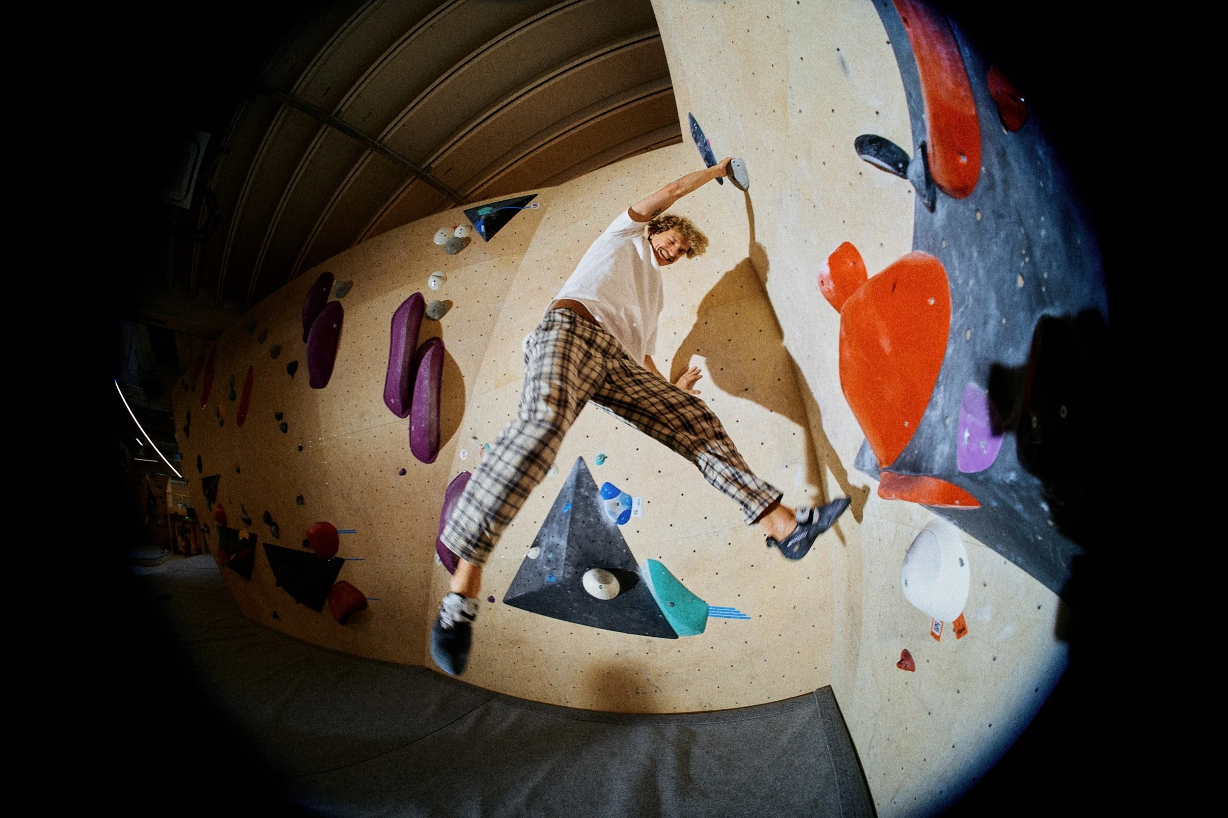Junge beim Bouldern in einer Indoor-Kletterhalle, an einer Wand mit bunten Klettergriffen.